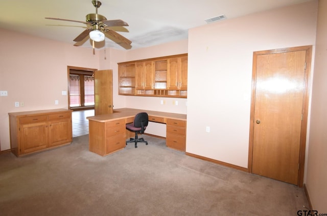 unfurnished office with built in desk, light colored carpet, and ceiling fan