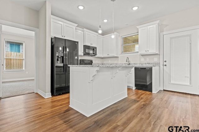 kitchen featuring a kitchen island, pendant lighting, white cabinets, and black appliances