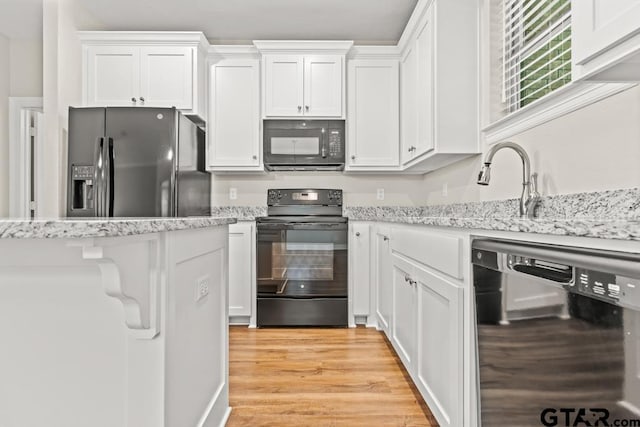 kitchen featuring white cabinetry, light stone counters, black appliances, and light hardwood / wood-style floors