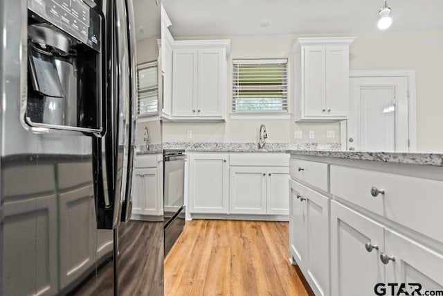 kitchen with sink, black fridge with ice dispenser, white cabinets, and light wood-type flooring