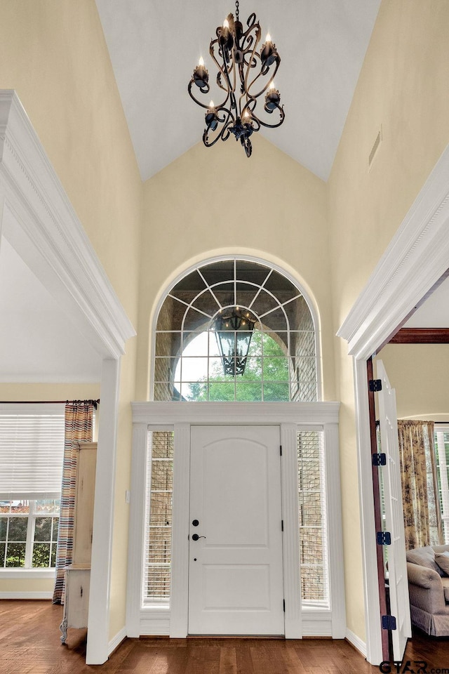 foyer entrance with a wealth of natural light, wood finished floors, a notable chandelier, and high vaulted ceiling