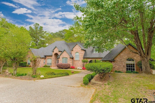 french country home with brick siding, a shingled roof, and a front yard