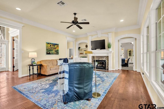 living area featuring visible vents, a ceiling fan, wood finished floors, arched walkways, and a premium fireplace