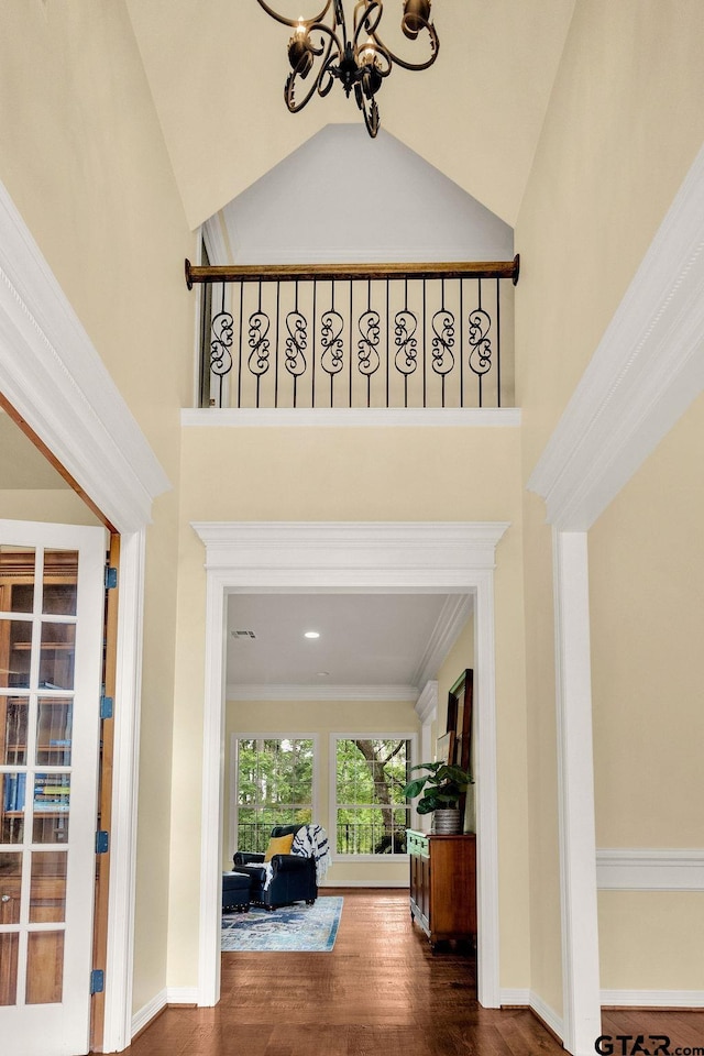 foyer with an inviting chandelier, high vaulted ceiling, crown molding, and wood finished floors