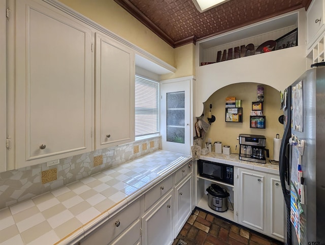601 Troup Hwy, Tyler, TX 75701 - kitchen featuring tile countertops, freestanding refrigerator, brick patterned floors, white cabinetry, and crown molding