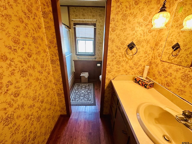 bathroom featuring wallpapered walls, wood finished floors, toilet, and vanity