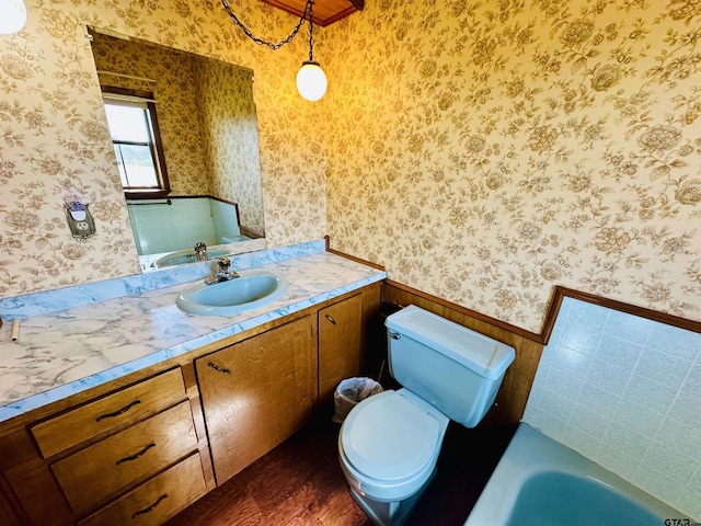 bathroom featuring wallpapered walls, a tub, toilet, wainscoting, and vanity