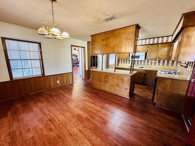 kitchen with white microwave, wallpapered walls, dark wood finished floors, light countertops, and wainscoting