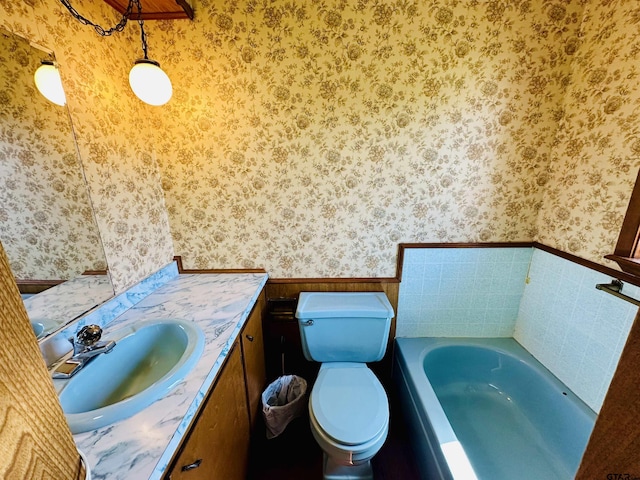 full bathroom featuring wallpapered walls, a wainscoted wall, toilet, a garden tub, and vanity