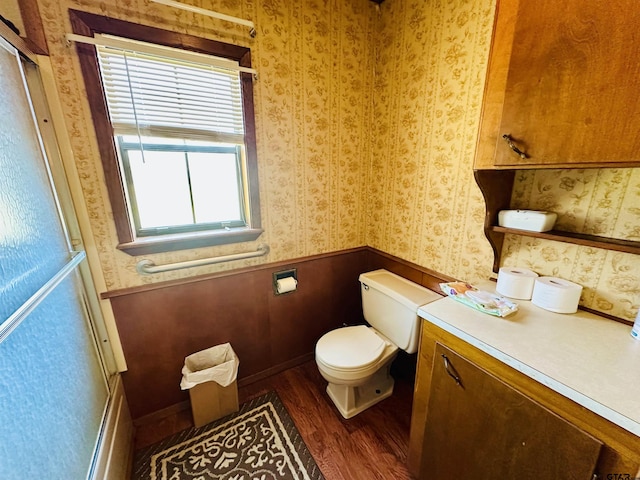 bathroom with toilet, wood finished floors, wainscoting, and wallpapered walls