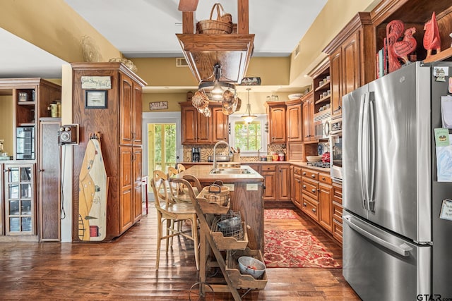 kitchen featuring a center island with sink, appliances with stainless steel finishes, dark hardwood / wood-style floors, decorative backsplash, and sink