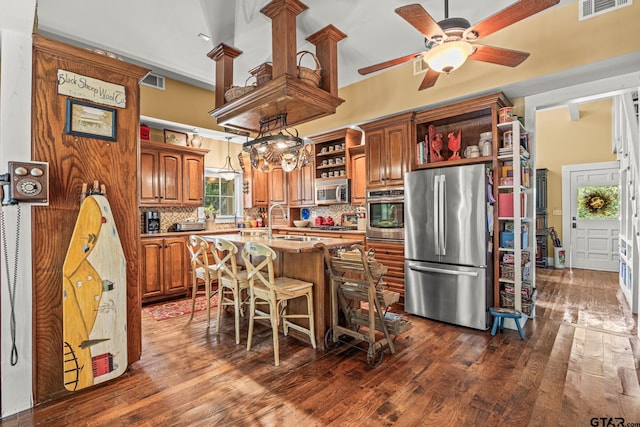 kitchen featuring a center island with sink, appliances with stainless steel finishes, a breakfast bar area, backsplash, and dark wood-type flooring