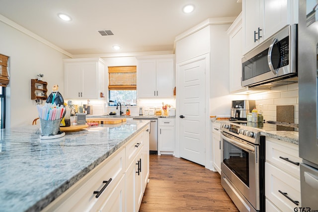 kitchen with light stone countertops, backsplash, stainless steel appliances, light hardwood / wood-style floors, and white cabinetry