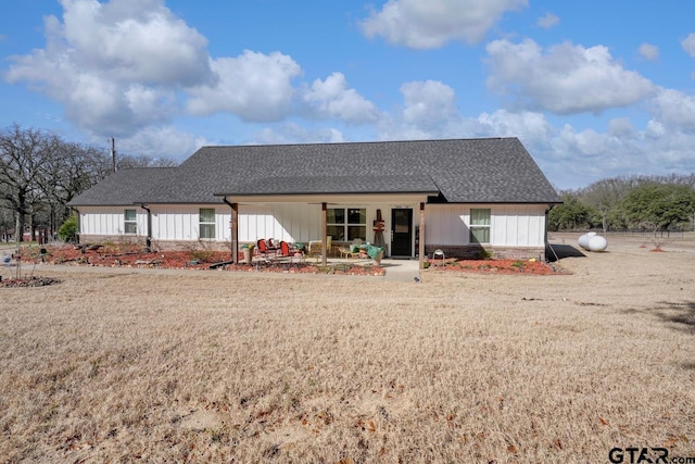 rear view of house with board and batten siding, roof with shingles, brick siding, and a lawn