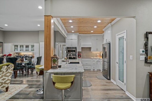 kitchen featuring wooden ceiling, light hardwood / wood-style flooring, light stone counters, white cabinetry, and stainless steel appliances