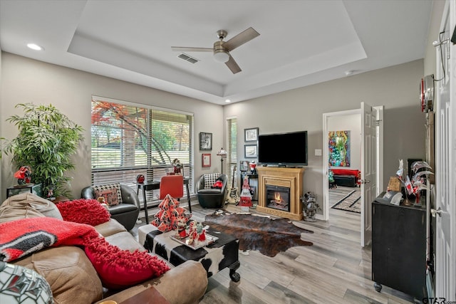 living room with a raised ceiling, ceiling fan, and light hardwood / wood-style floors