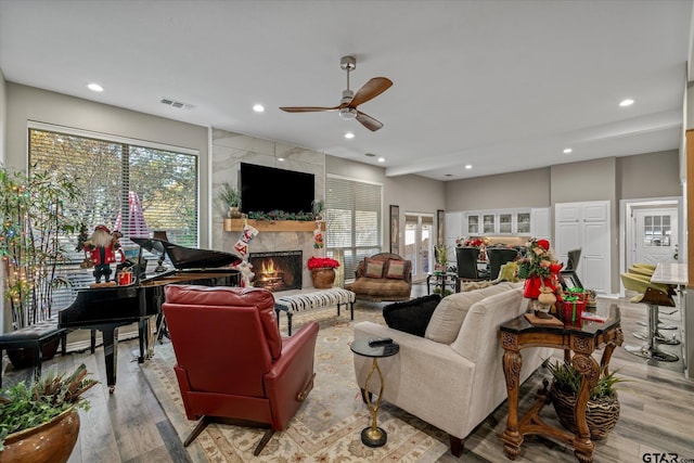 living room with a tiled fireplace, ceiling fan, plenty of natural light, and light wood-type flooring