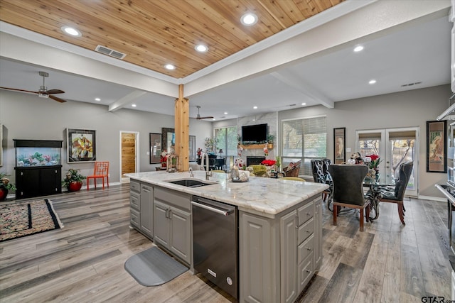 kitchen with ceiling fan, light stone counters, light hardwood / wood-style flooring, gray cabinets, and a center island with sink