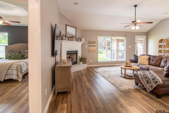 living room with wood-type flooring, vaulted ceiling, a brick fireplace, and a wealth of natural light