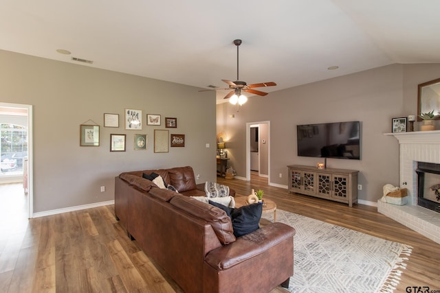 living room featuring ceiling fan, vaulted ceiling, a brick fireplace, and light hardwood / wood-style flooring