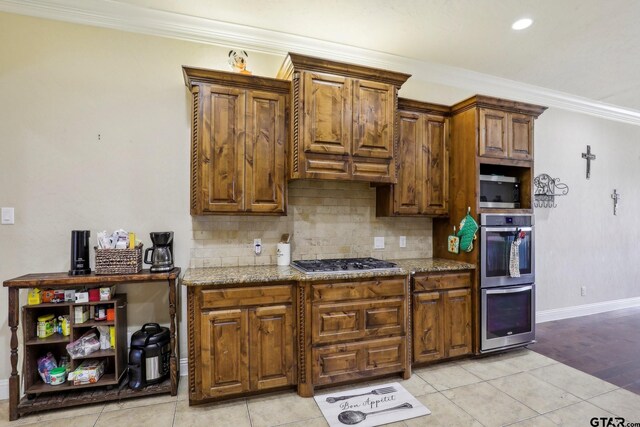3449 Abes Landing Dr, Granbury, TX 76049 - kitchen with stainless steel appliances, ornamental molding, decorative backsplash, light tile patterned floors, and brown cabinetry