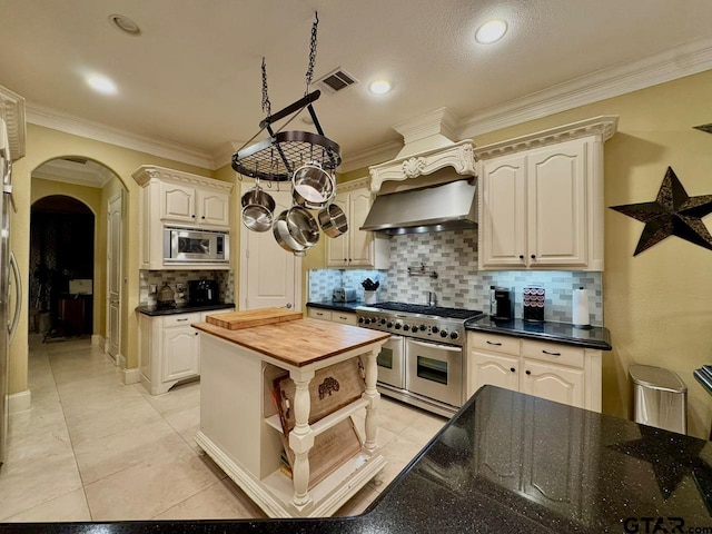 kitchen featuring crown molding, stainless steel appliances, wooden counters, and wall chimney exhaust hood