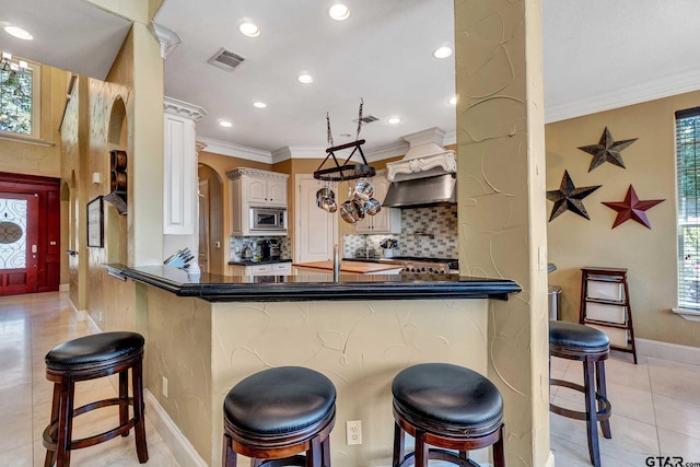 kitchen featuring stainless steel microwave, ornamental molding, kitchen peninsula, and a kitchen bar