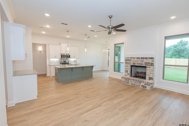 kitchen with light stone countertops, appliances with stainless steel finishes, ceiling fan, white cabinetry, and hanging light fixtures