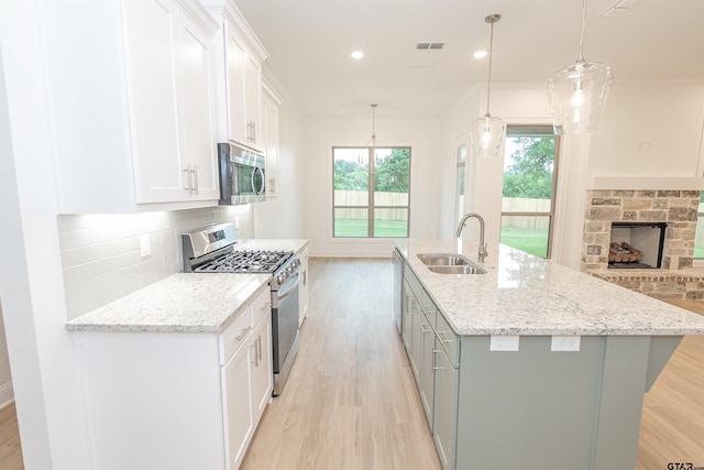 kitchen with stainless steel appliances, sink, white cabinets, hanging light fixtures, and an island with sink