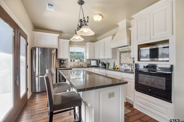 kitchen with dark hardwood / wood-style flooring, a center island, hanging light fixtures, appliances with stainless steel finishes, and premium range hood