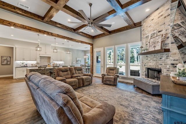 living room with a brick fireplace, hardwood / wood-style flooring, beam ceiling, and coffered ceiling