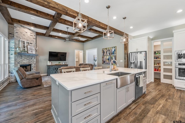 kitchen with a fireplace, appliances with stainless steel finishes, dark hardwood / wood-style floors, sink, and an island with sink