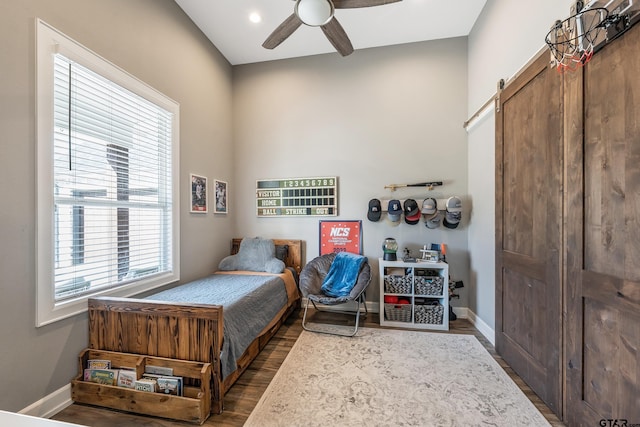 bedroom with dark wood-type flooring, a barn door, and ceiling fan