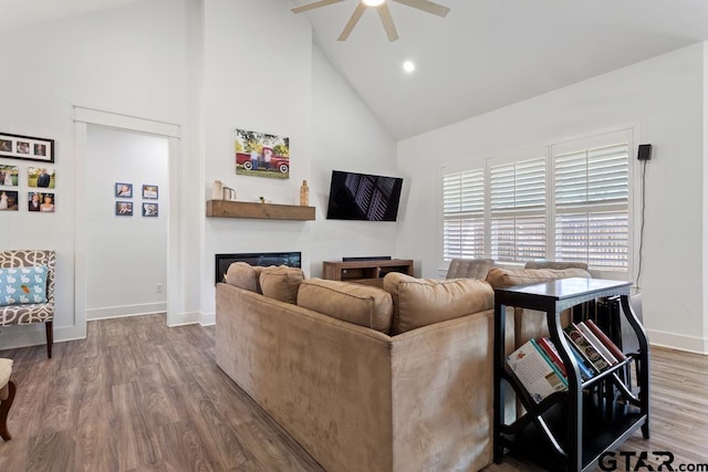 living area featuring wood finished floors, baseboards, high vaulted ceiling, ceiling fan, and a glass covered fireplace