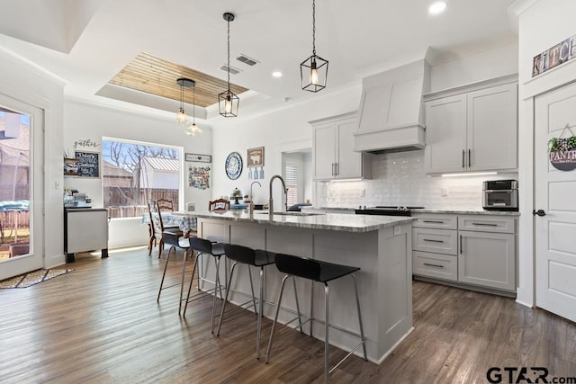 kitchen with light stone countertops, a sink, custom range hood, a raised ceiling, and backsplash