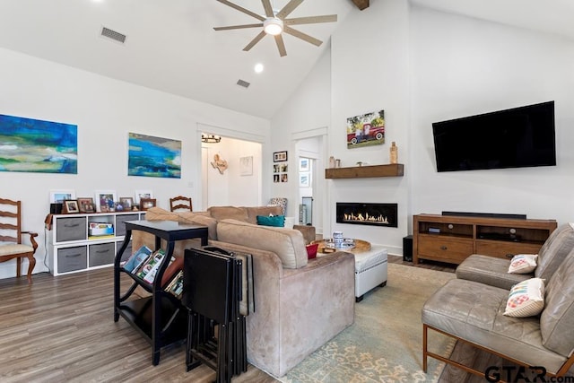 living area with wood finished floors, visible vents, a warm lit fireplace, and high vaulted ceiling