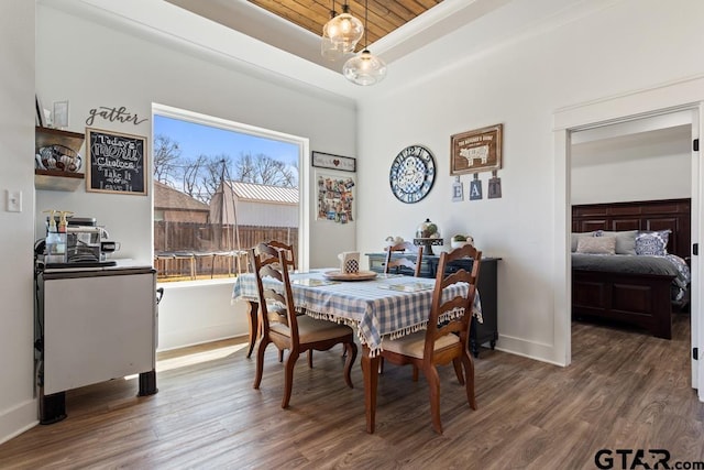 dining room with an inviting chandelier, a raised ceiling, baseboards, and wood finished floors