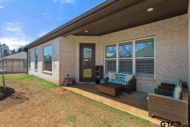 view of exterior entry with an outdoor living space, a patio, fence, a yard, and brick siding