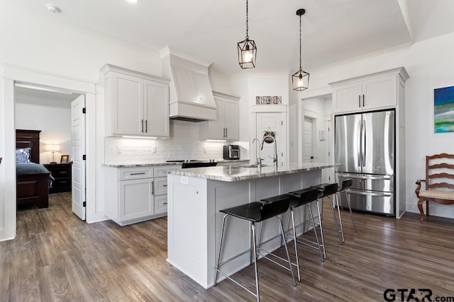 kitchen with dark wood finished floors, custom range hood, decorative backsplash, freestanding refrigerator, and a sink