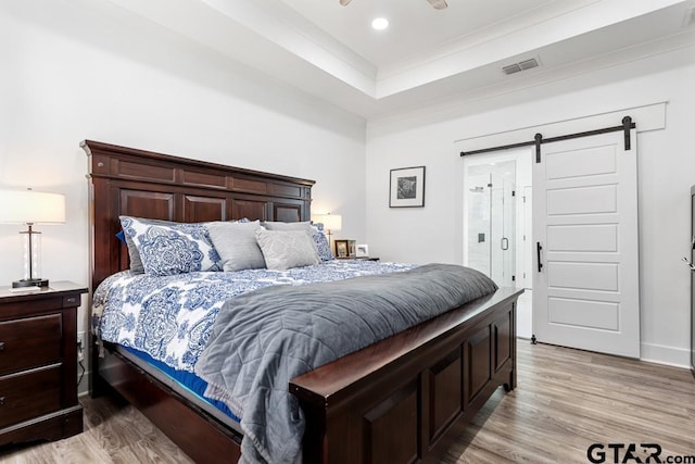 bedroom with visible vents, a barn door, recessed lighting, light wood-style flooring, and a raised ceiling