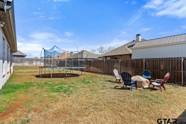 view of yard featuring a trampoline, a fenced backyard, and an outdoor fire pit