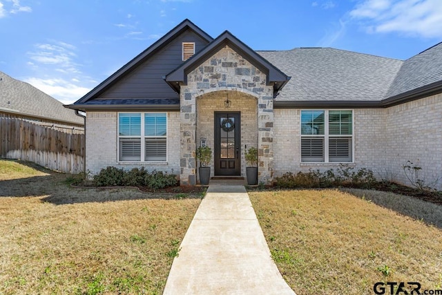 view of front of home featuring a front yard, fence, brick siding, and a shingled roof