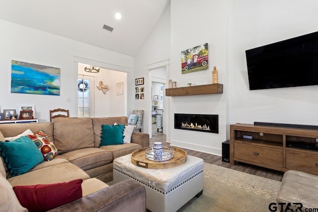 living area with visible vents, recessed lighting, a warm lit fireplace, wood finished floors, and high vaulted ceiling