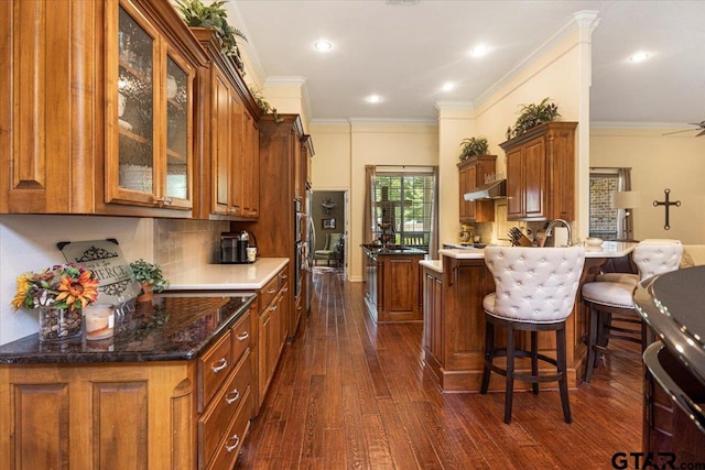909 Univerity Dr, Carthage, TX 75633 - kitchen with brown cabinetry, dark wood finished floors, backsplash, glass insert cabinets, and under cabinet range hood