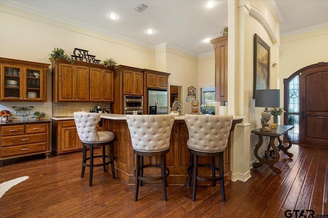 909 Univerity Dr, Carthage, TX 75633 - kitchen with stainless steel appliances, brown cabinets, dark wood finished floors, glass insert cabinets, and ornamental molding