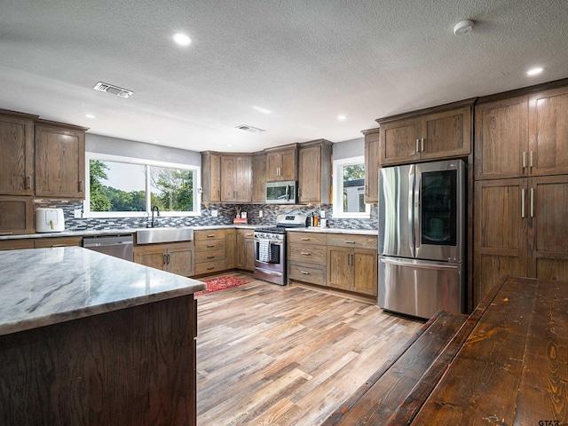 kitchen featuring tasteful backsplash, light wood-type flooring, appliances with stainless steel finishes, and light stone countertops