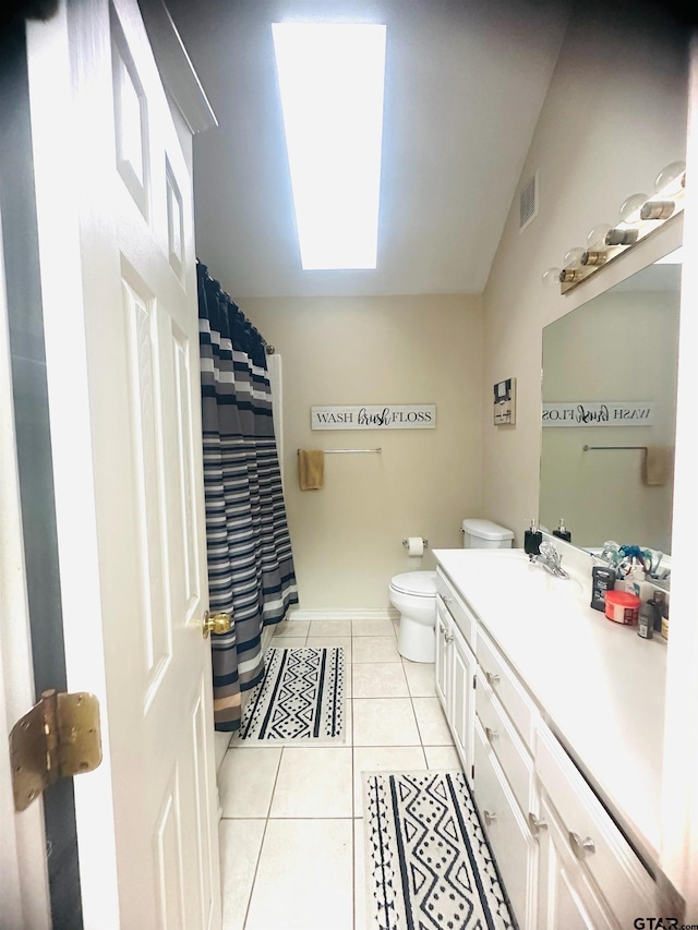 bathroom with toilet, vaulted ceiling with skylight, vanity, and tile patterned floors