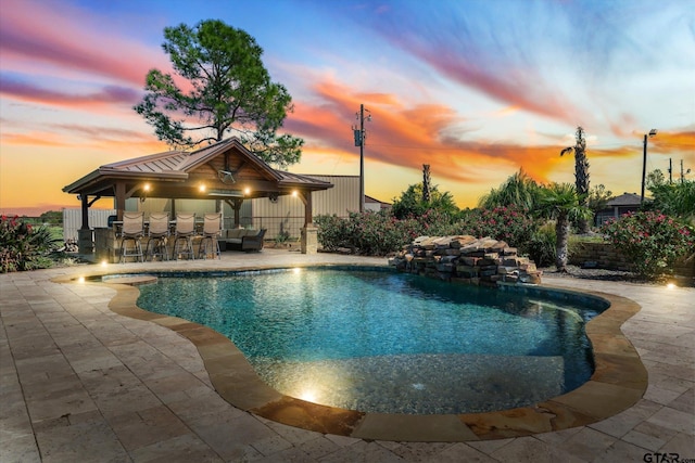 pool at dusk with exterior bar, a patio, and a gazebo