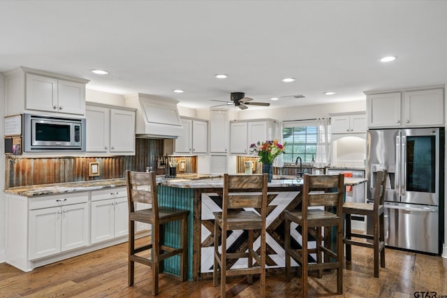 kitchen featuring stainless steel appliances, ceiling fan, custom exhaust hood, wood-type flooring, and white cabinets