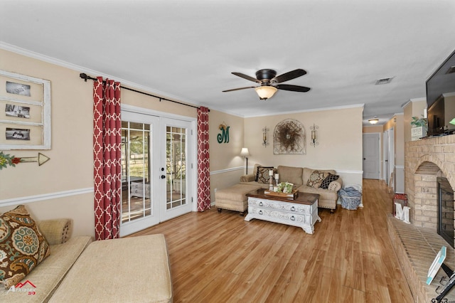 living room featuring a brick fireplace, wood-type flooring, ornamental molding, and french doors